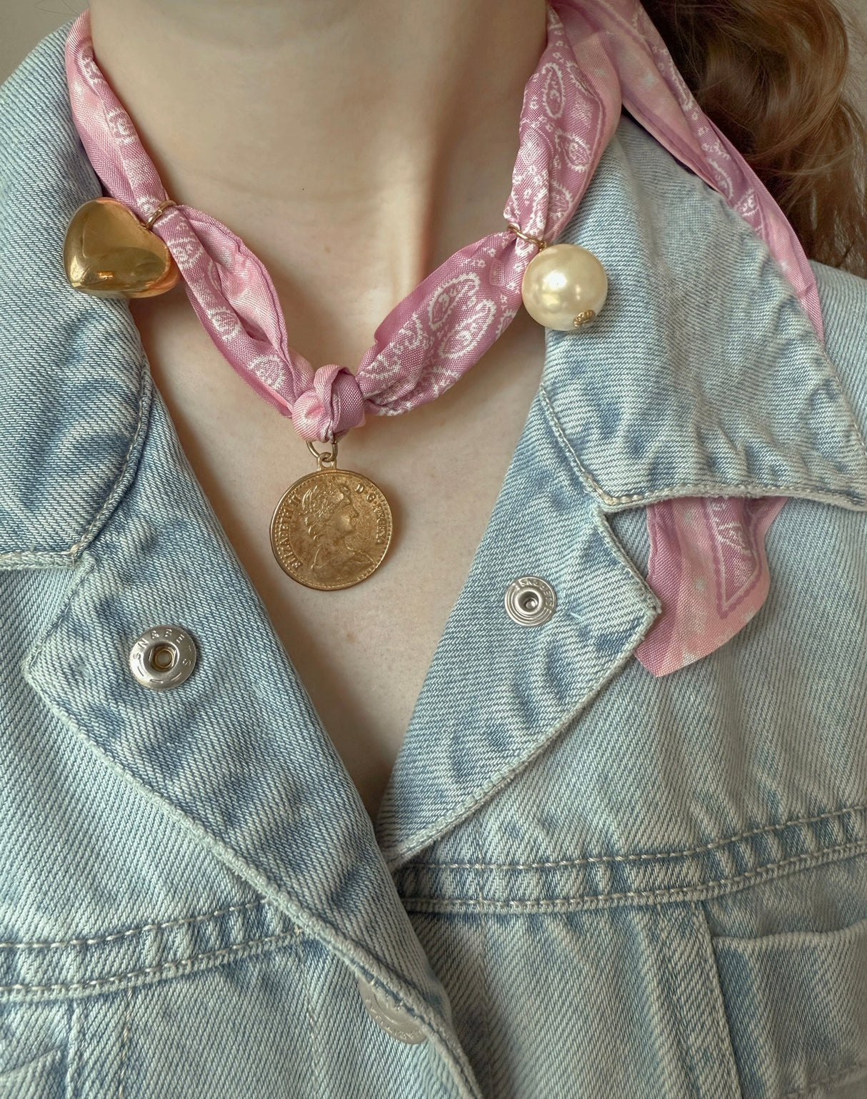 A person wearing the Portofino Scarf Necklace by Kinsey Designs, featuring charms and a coin pendant, paired with a light denim jacket.