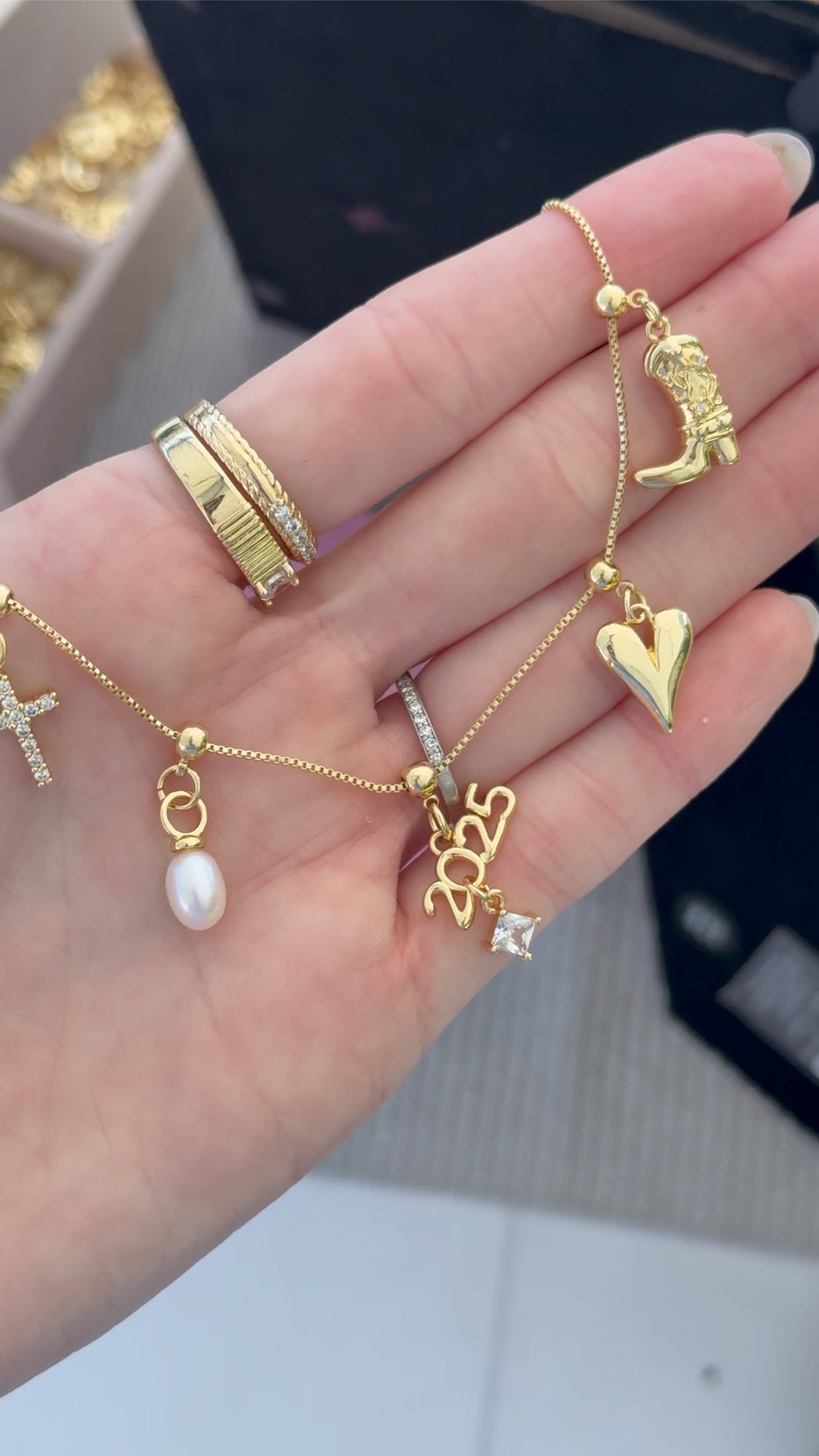 A hand holds the Kinsey Designs Archives 2025 Graduation Grip Charm—a gold bracelet with heart, pearl, star, and shoe charms—ideal for commemorating graduation or pairing with Kinsey Charm Bar Necklaces.