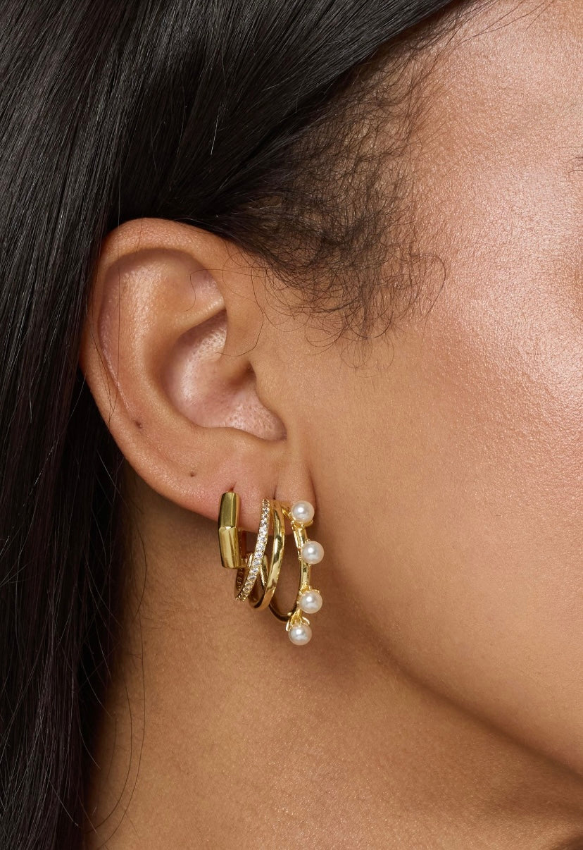Close-up of a woman's ear wearing four Kinsey Designs gold-filled hoop earrings, including Hattie Pearl Hoops and a stylish triple-layered design.