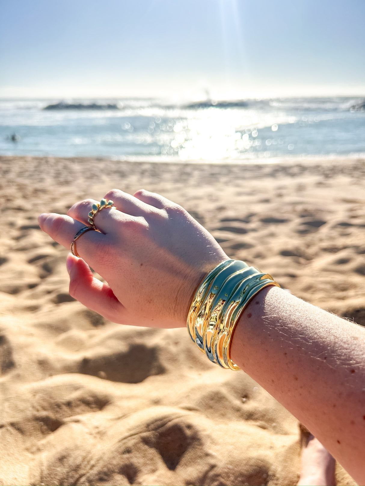 An image of a person on a beach showing off their cuff bracelet and also has beautiful gold rings