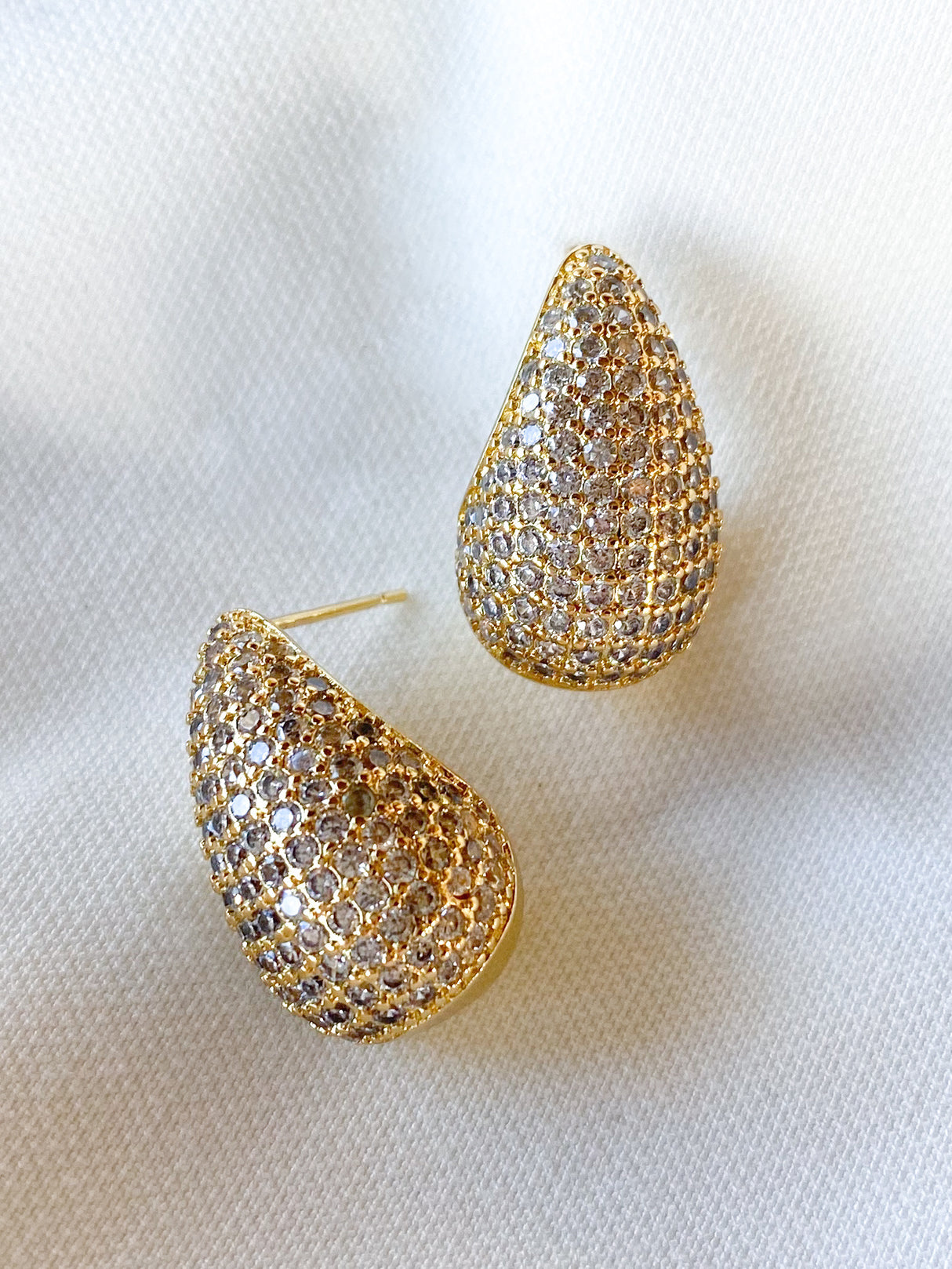 The Alice Earrings by Kinsey Designs are gold-filled, teardrop-shaped earrings with sparkling cubic zirconia rhinestones, shown on a white textured fabric background.
