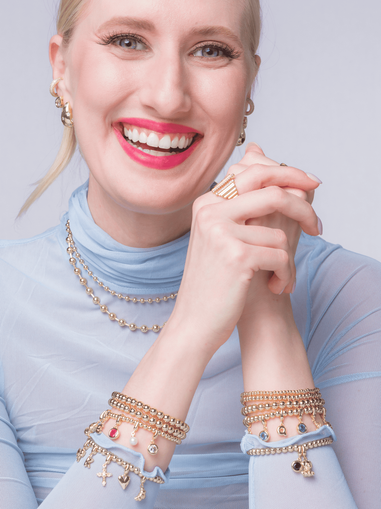 A smiling woman in a sheer blue top wears gold jewelry and colorful Kinsey Designs clip charms, including the Eiffel Tower Clip Charm featuring a secure hinged clasp.