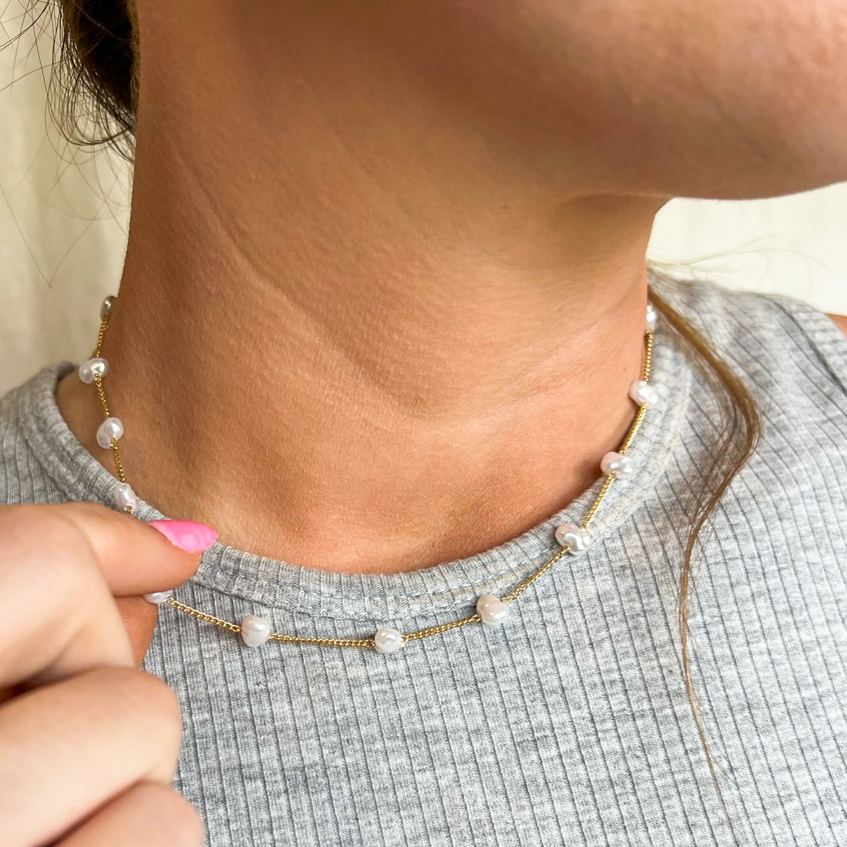 Close-up of a woman wearing the Adalee gold-plated necklace with small white pearls by Kinsey Designs Archives, gently holding it with her hand.
