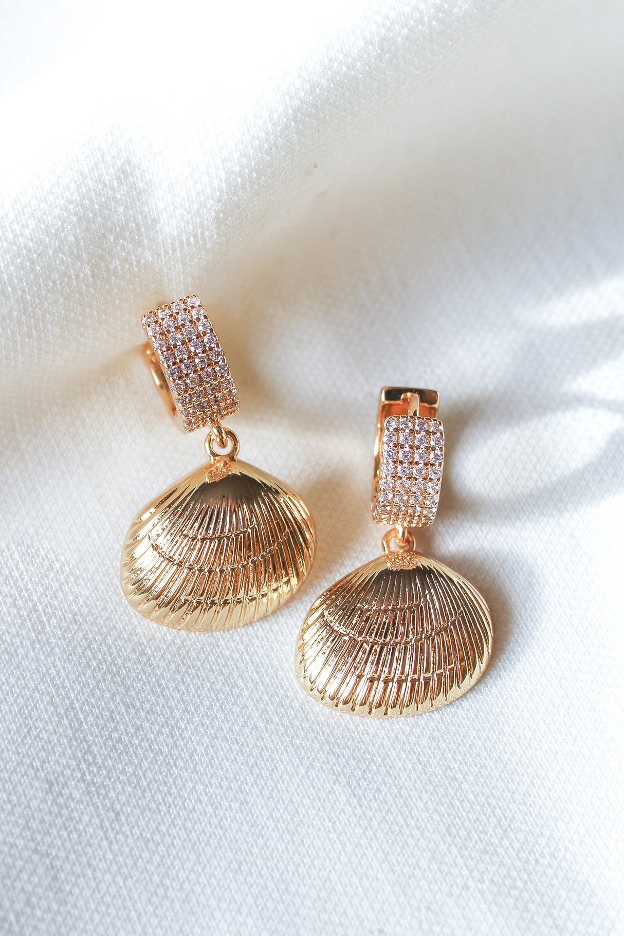 The Alana Huggies by Kinsey Designs Archives feature gold-filled, seashell-inspired texture and are displayed on a white fabric backdrop—a standout pick for any sample sale.