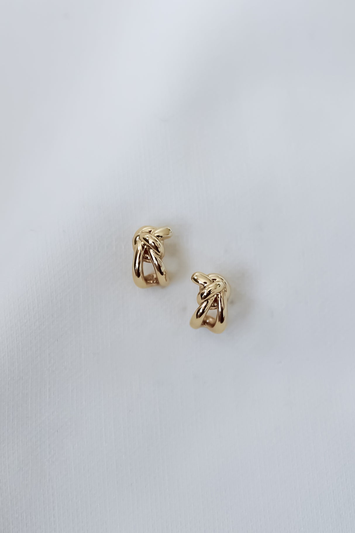 The Ana Stud Small earrings by Kinsey Designs are two petite, gold-filled knot studs, each measuring 0.25" long, shown against a white fabric background.