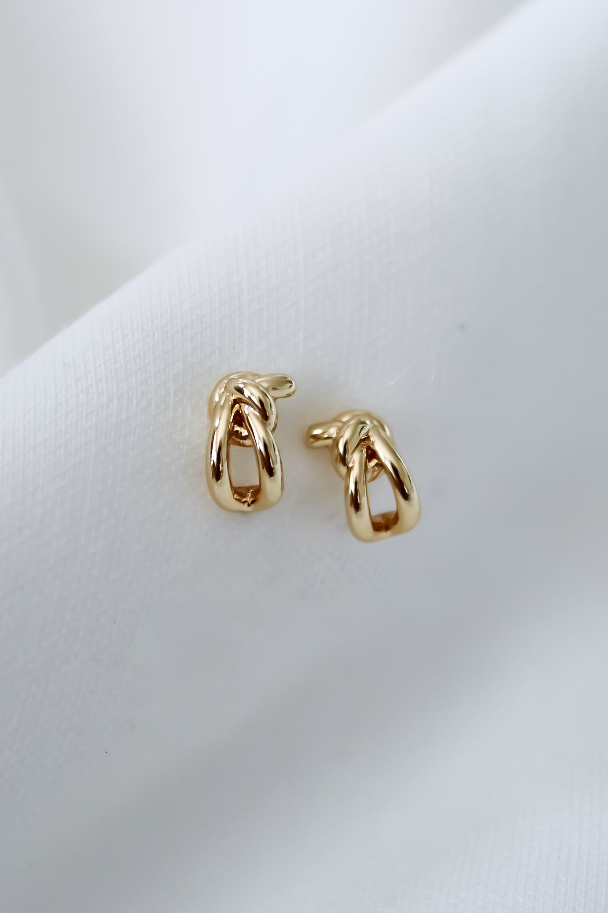 The Ana Stud Small by Kinsey Designs are gold filled knot-shaped earrings, .25" long, shown on a soft white fabric background.