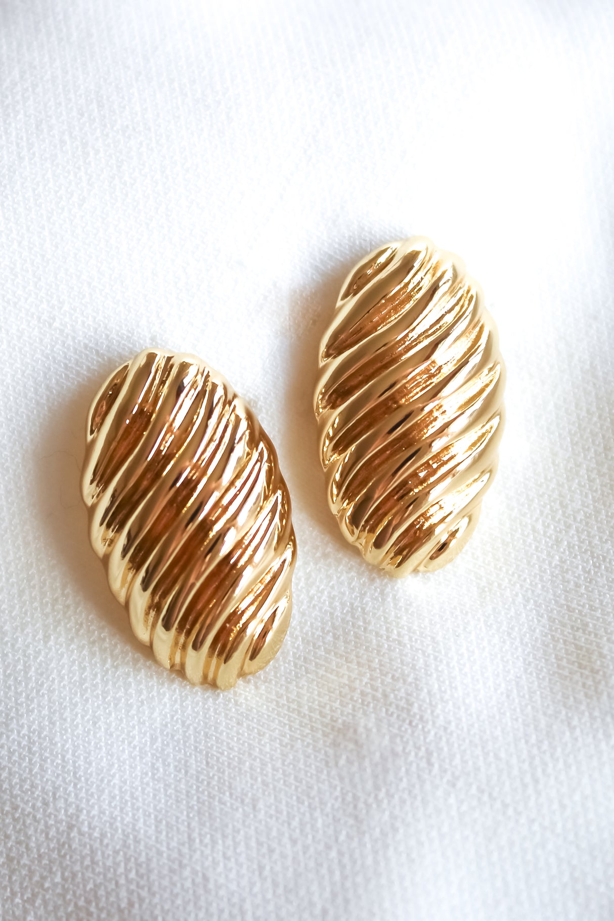 The Annette Earring by Kinsey Designs Archives features gold-filled, ribbed, oval-shaped 1-inch earrings, displayed on a soft white fabric background.