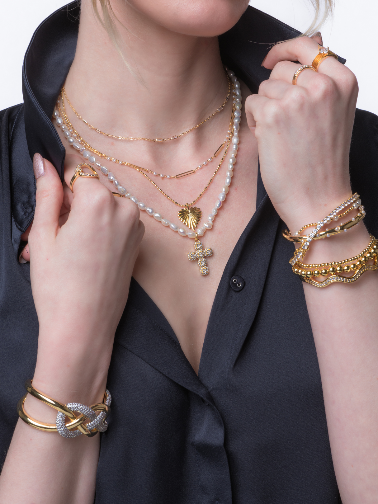 A woman in a black shirt wears layered gold and pearl necklaces, rings, and the Arthur Tennis Bracelet by Kinsey Designs—an elegant accessory that makes a perfect gift for her.