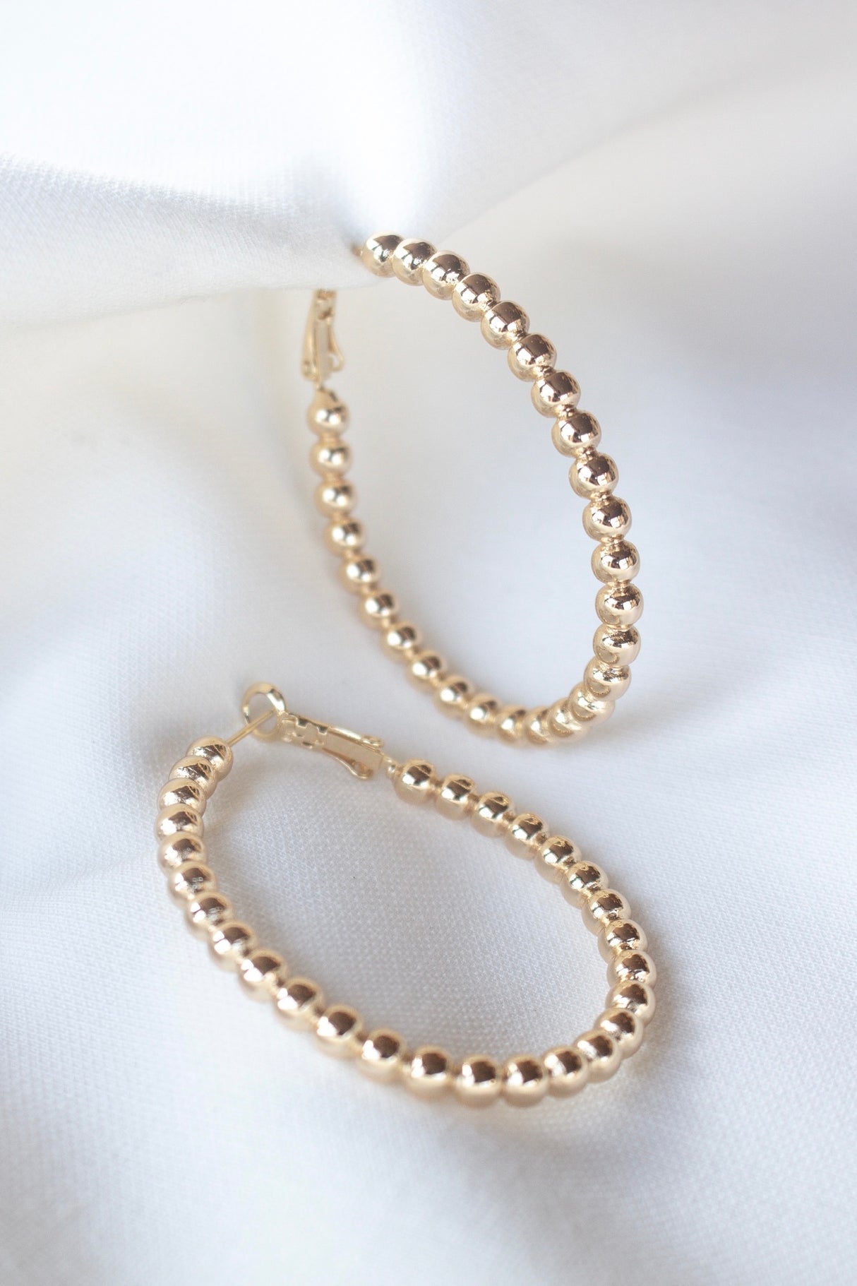 The Atlas Hoop by Kinsey Designs Archives, shown on a white fabric background, adds timeless elegance to any look—shop this exclusive sample sale now.