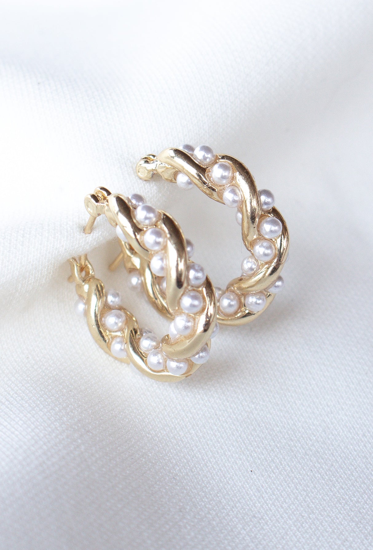 Audrey Pearl Hoops by Kinsey Designs: Gold hoop earrings with a twisted design, accented with small white pearls and shown on a white fabric background.