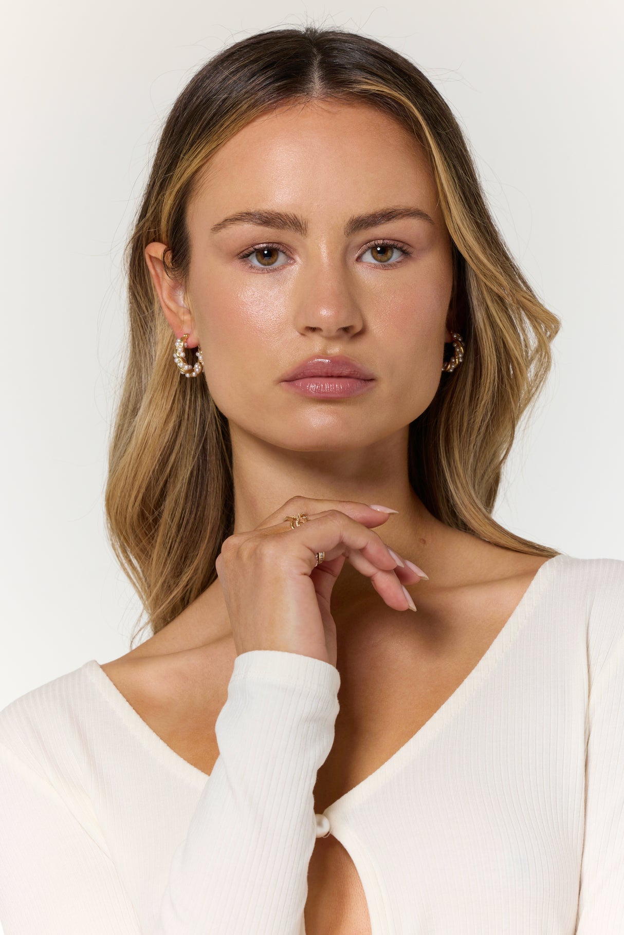 A woman with long blonde hair and a white top wears Kinsey Designs’ Audrey Pearl Hoops, gazing directly at the camera.