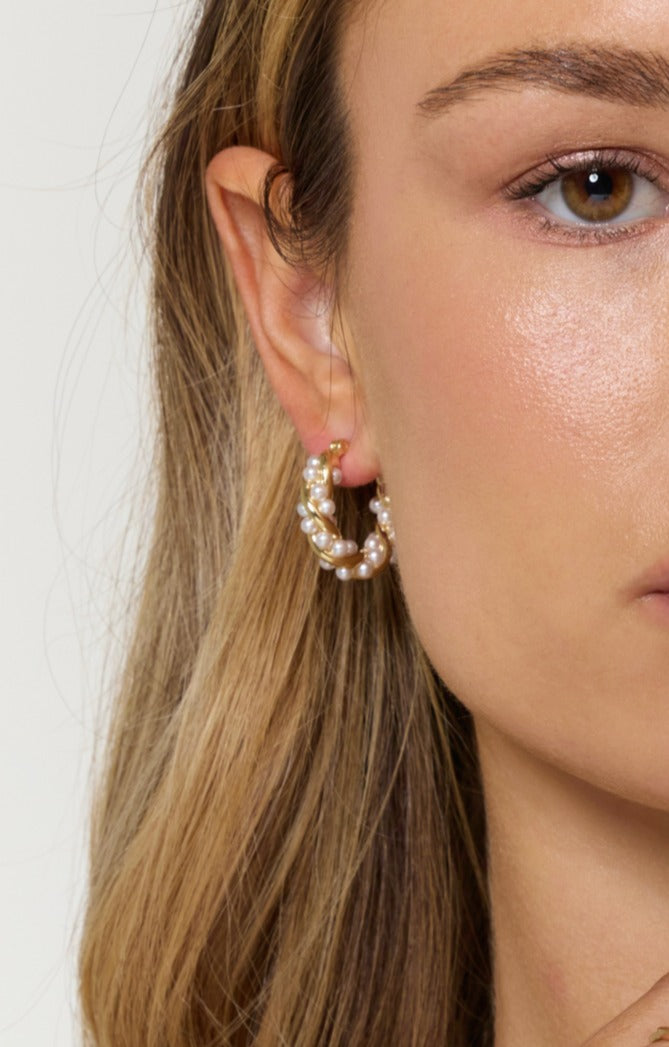 Close-up of a woman wearing Kinsey Designs' Audrey Pearl Hoops, gold earrings accented with small pearls, partially showing her face and hair.