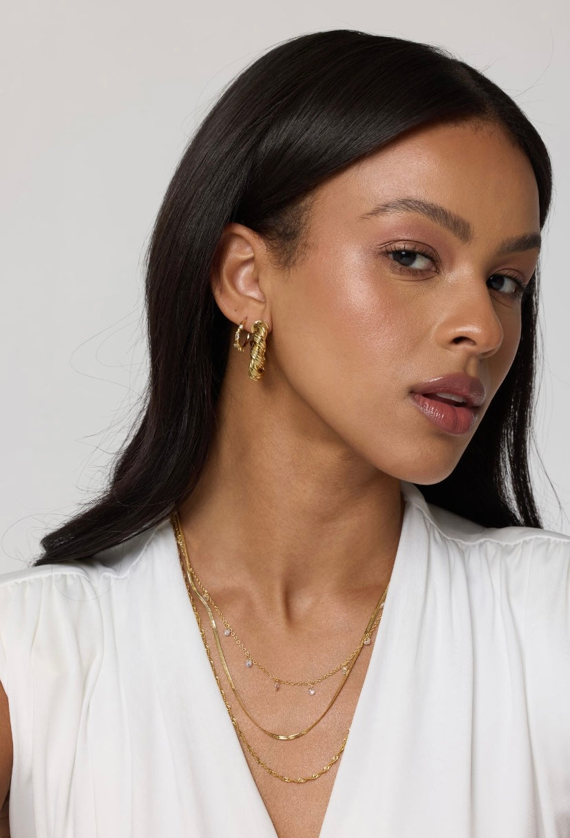 Woman with long dark hair wears Kinsey Designs' Chase Hoop Mini gold-filled layered necklaces, 0.5" diameter cubic zirconia gold earrings, and a white top, looking at the camera.