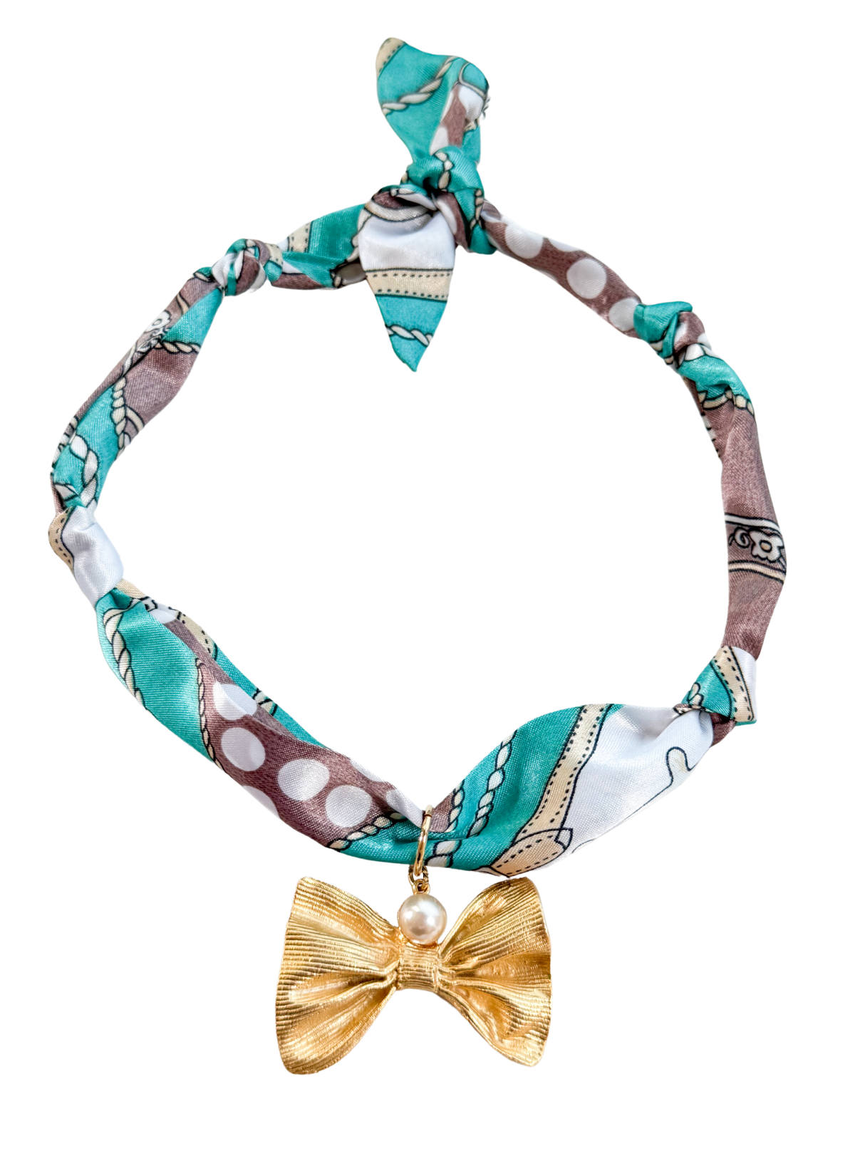 The Siena Scarf Necklace by Kinsey Designs features a chic teal, brown, and white pattern with an adjustable fit, finished with a gold bow and pearl pendant for vintage-inspired elegance.