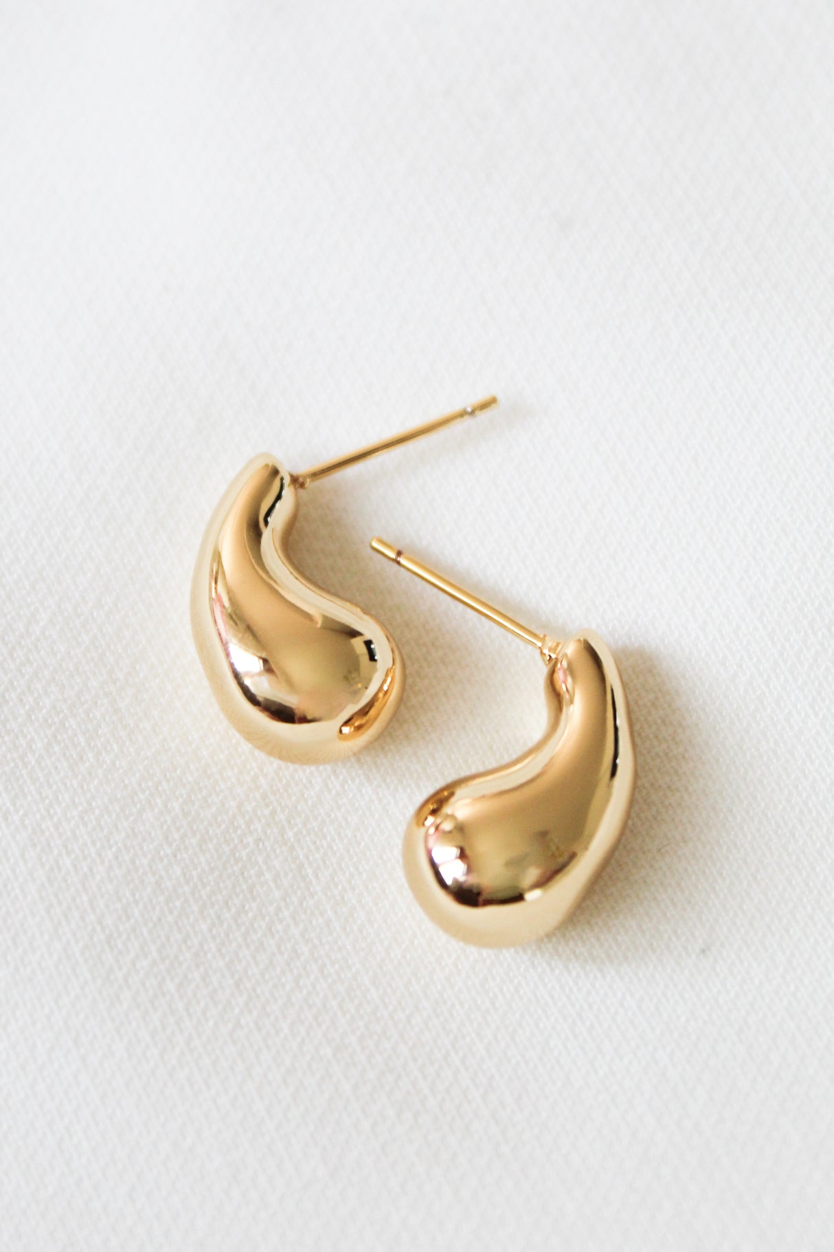 The Baby Drop Post by Kinsey Designs is a pair of gold filled, bean-shaped stud earrings measuring .75" long, shown on a white textured surface.