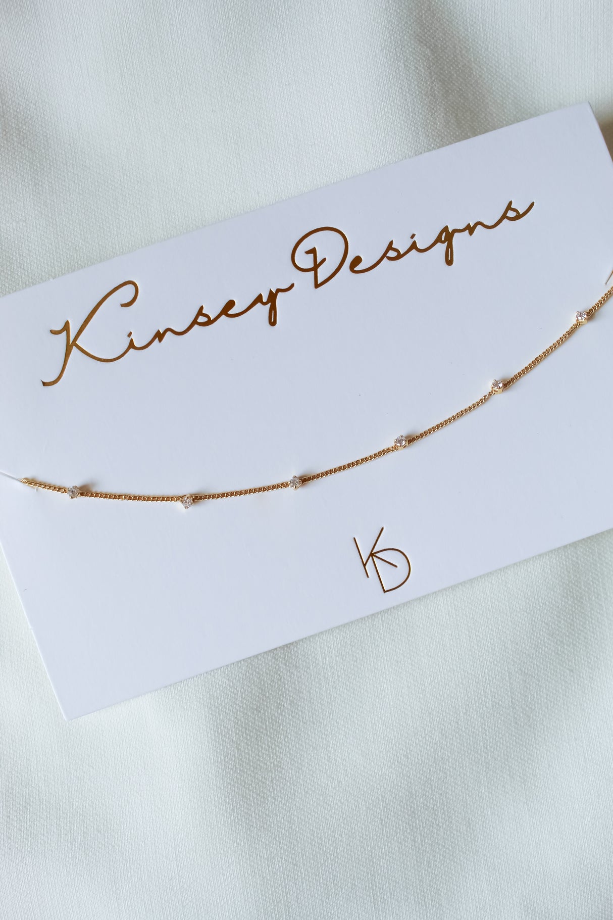 The Bailey Necklace by Kinsey Designs Archives features a delicate 16" gold chain with small beads, displayed on a branded card against a white fabric background. Final sale.