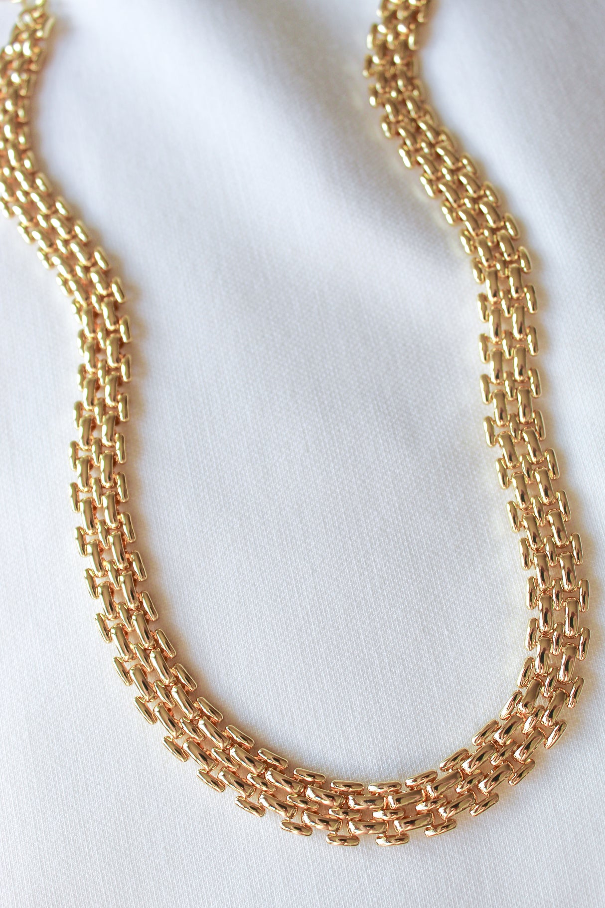 The Basque Necklace by Kinsey Designs Archives features a textured, chunky gold chain and is elegantly displayed on a white fabric background.
