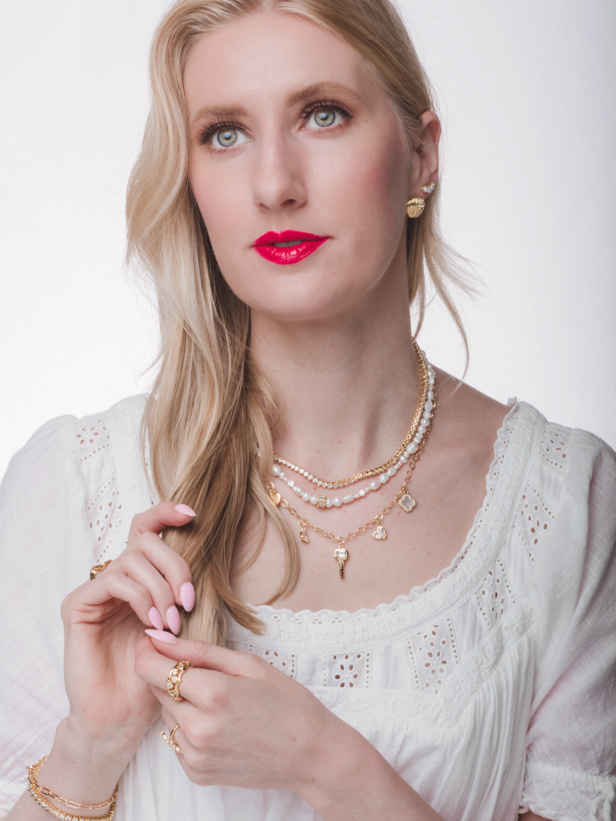 Blonde woman in a white top wears Kinsey Designs’ Beth Freshwater Pearl Necklace with layered gold and pearl jewelry and bright pink lipstick—this elegant piece makes the perfect bridesmaid gift.