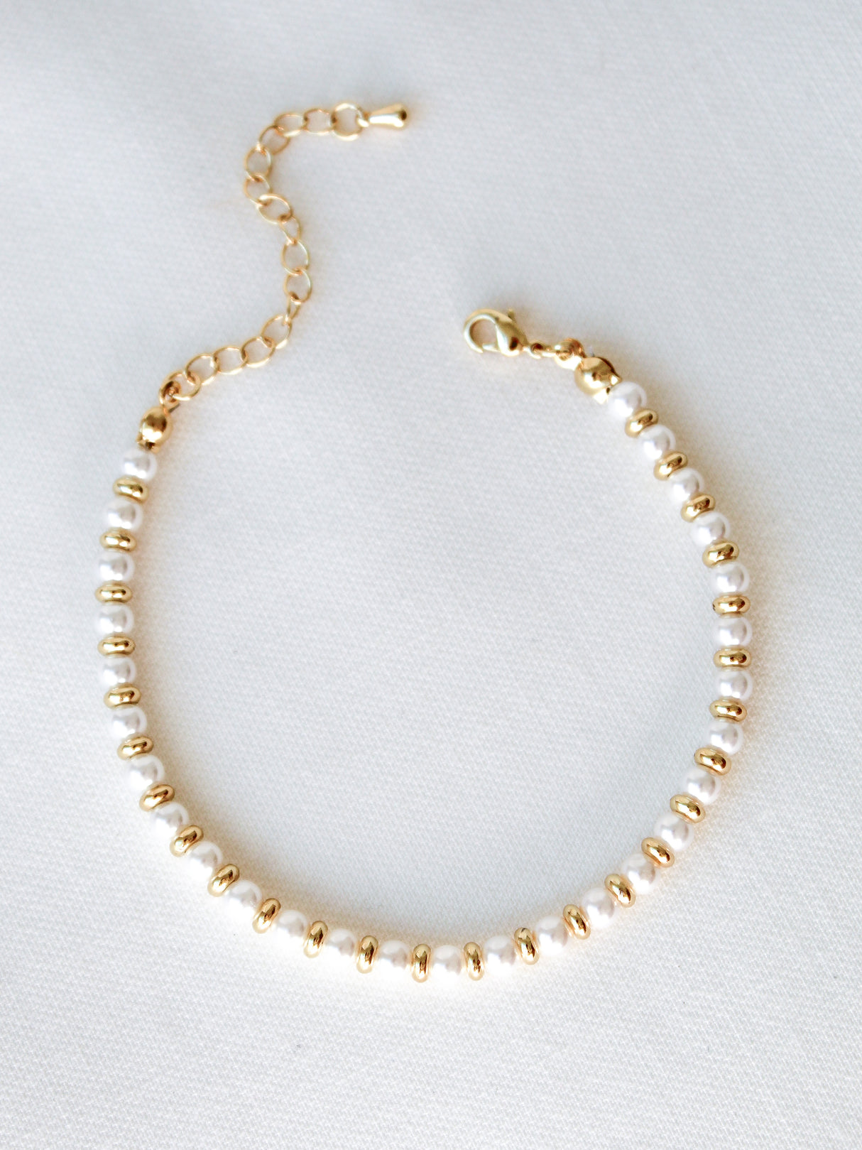 The Blakely Pearl Bracelet by Kinsey Designs features pearl beads on a gold filled adjustable 6.25" chain, elegantly displayed on a white fabric background.
