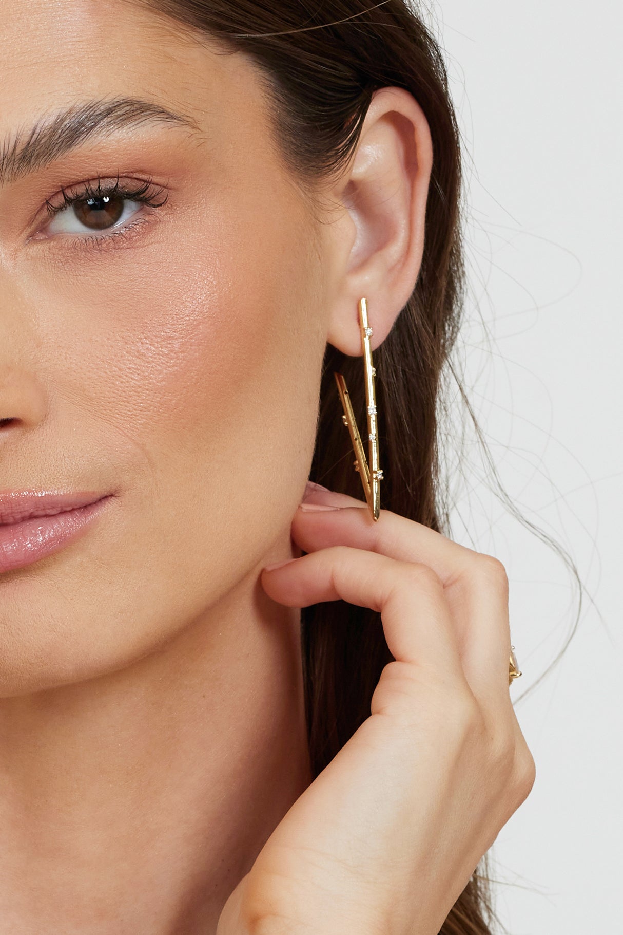 A woman with natural makeup touches her hair in a close-up while wearing Kinsey Designs' Bowen Earring Luxe gold-filled hoops.