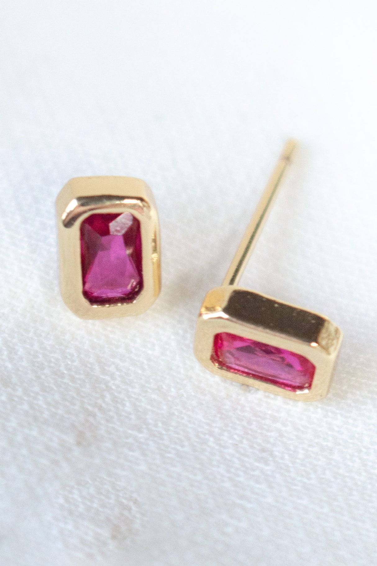 The Brooks Stud by Kinsey Designs Archives features gold stud earrings with rectangular pink gemstones, shown with a gold-filled ring on a white textured background—perfect for adding elegance to any look.