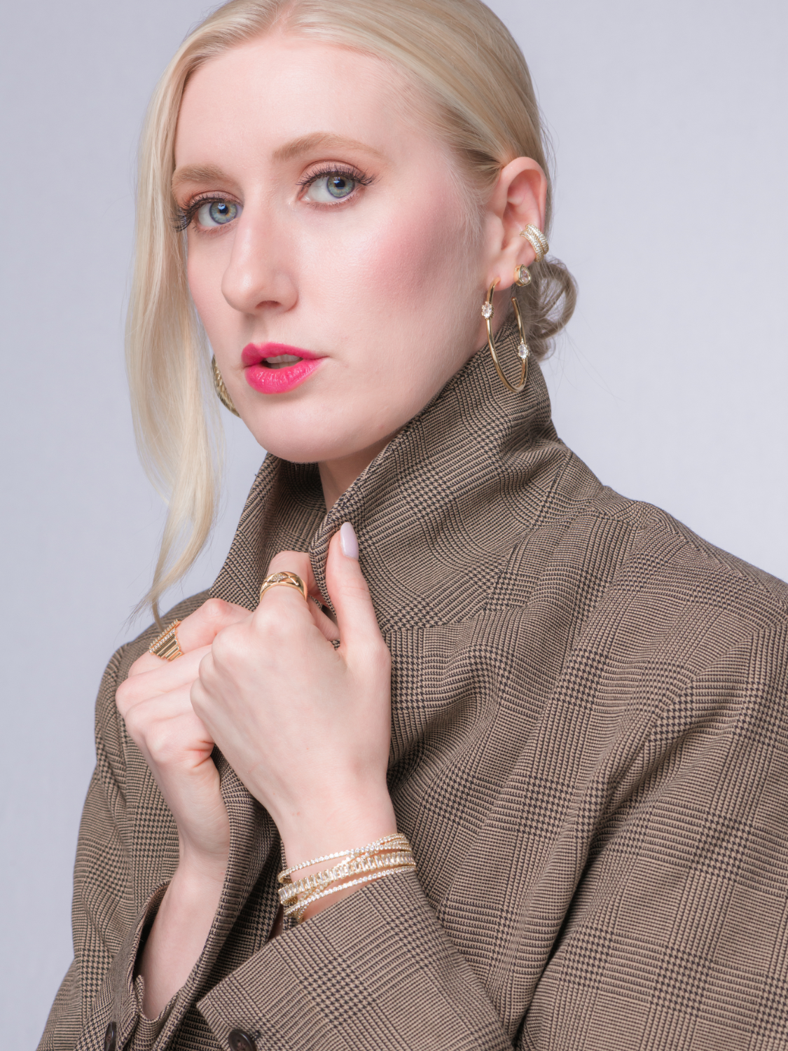 Woman with blonde hair in a brown plaid blazer wears the Clotho Hoop Earring by Kinsey Designs Archives and pink lipstick. A chic look for browsing a sample sale or choosing your final sale pick.
