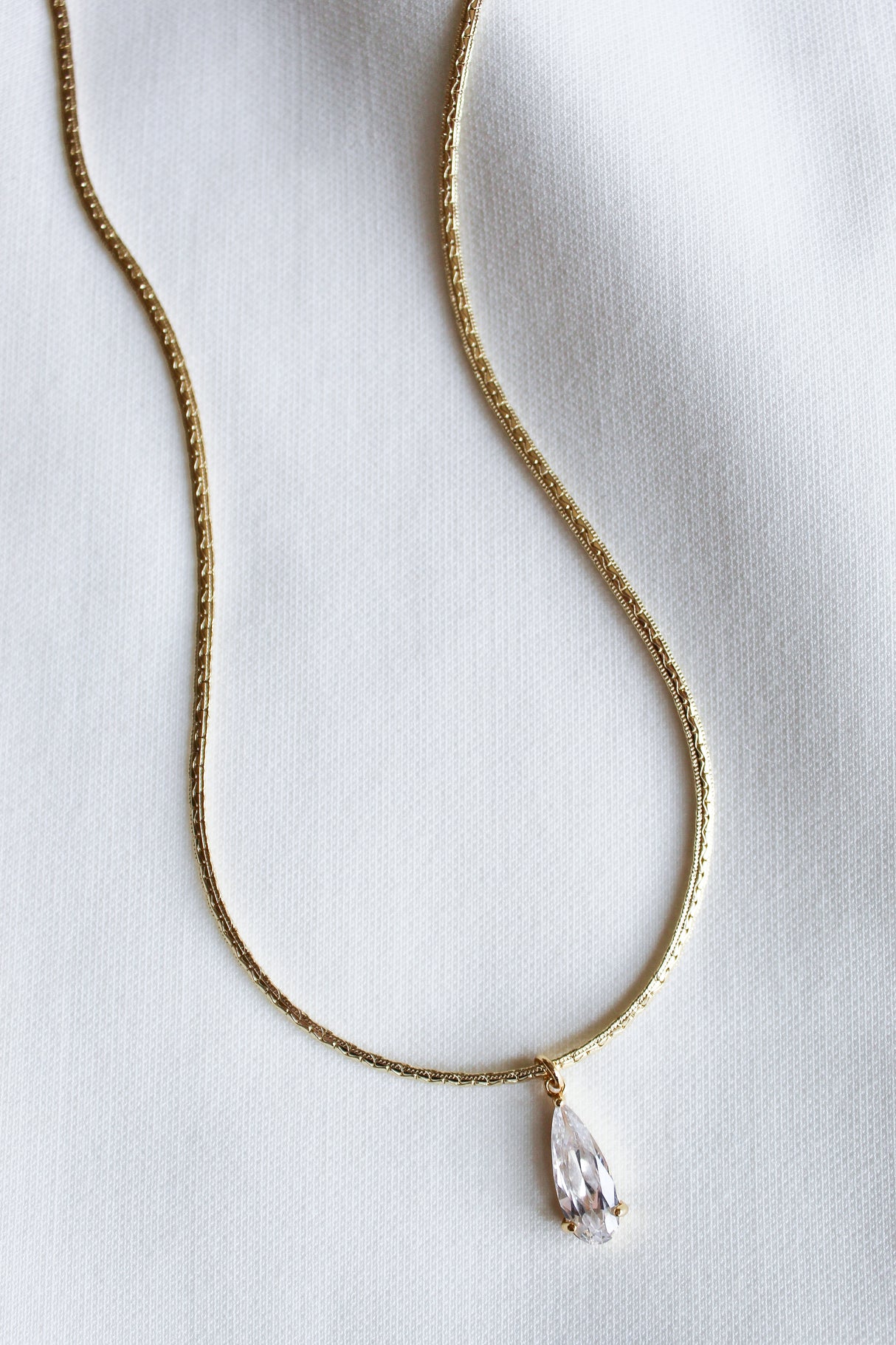 The Charlotte Drop Necklace by Kinsey Designs showcases a sparkling cubic zirconia teardrop pendant, elegantly displayed against a white fabric background.