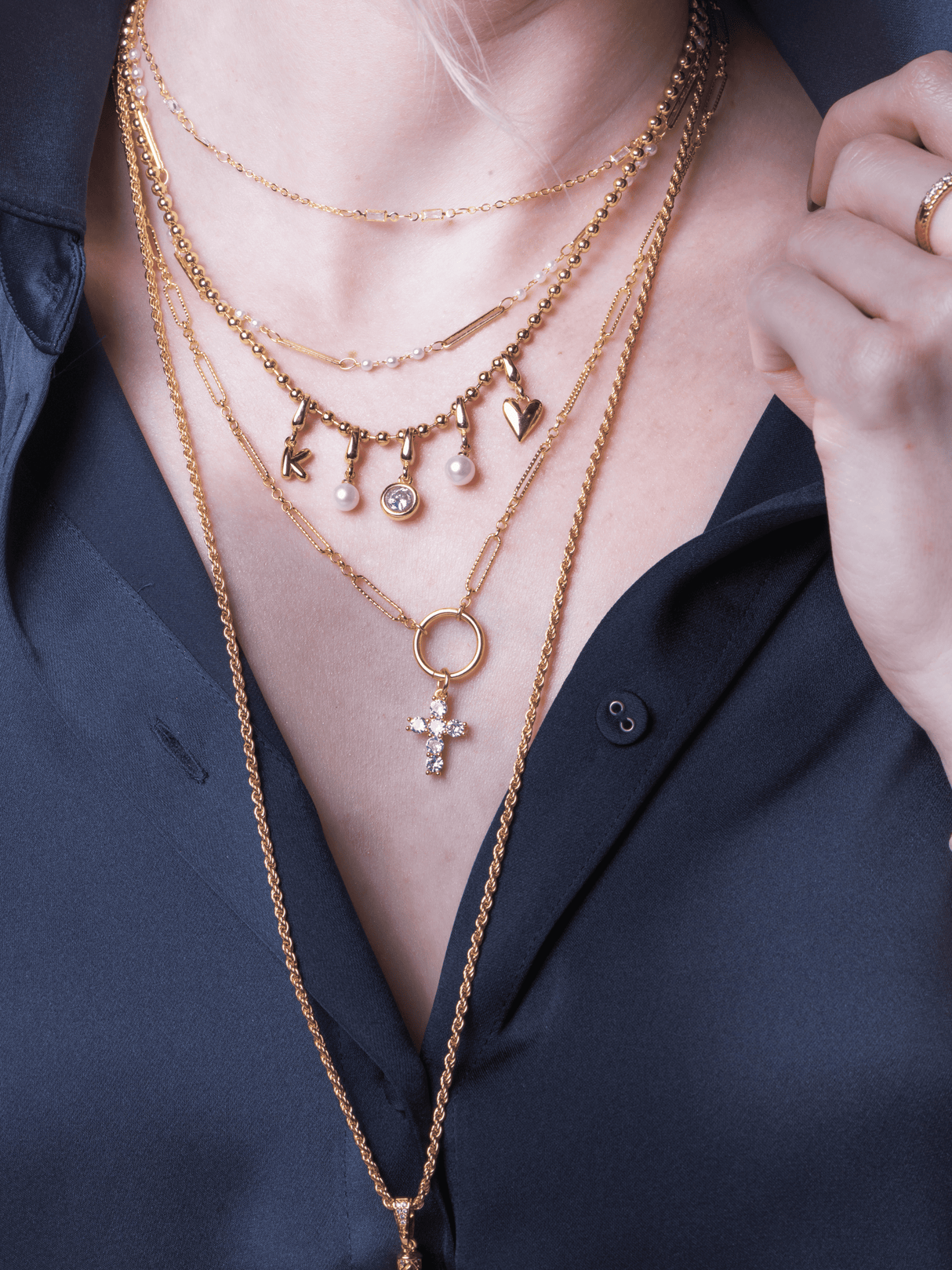 A woman in a dark blue shirt wears the Kinsey Designs Archives Charm Necklace Ball Chain, her hand near her collar.