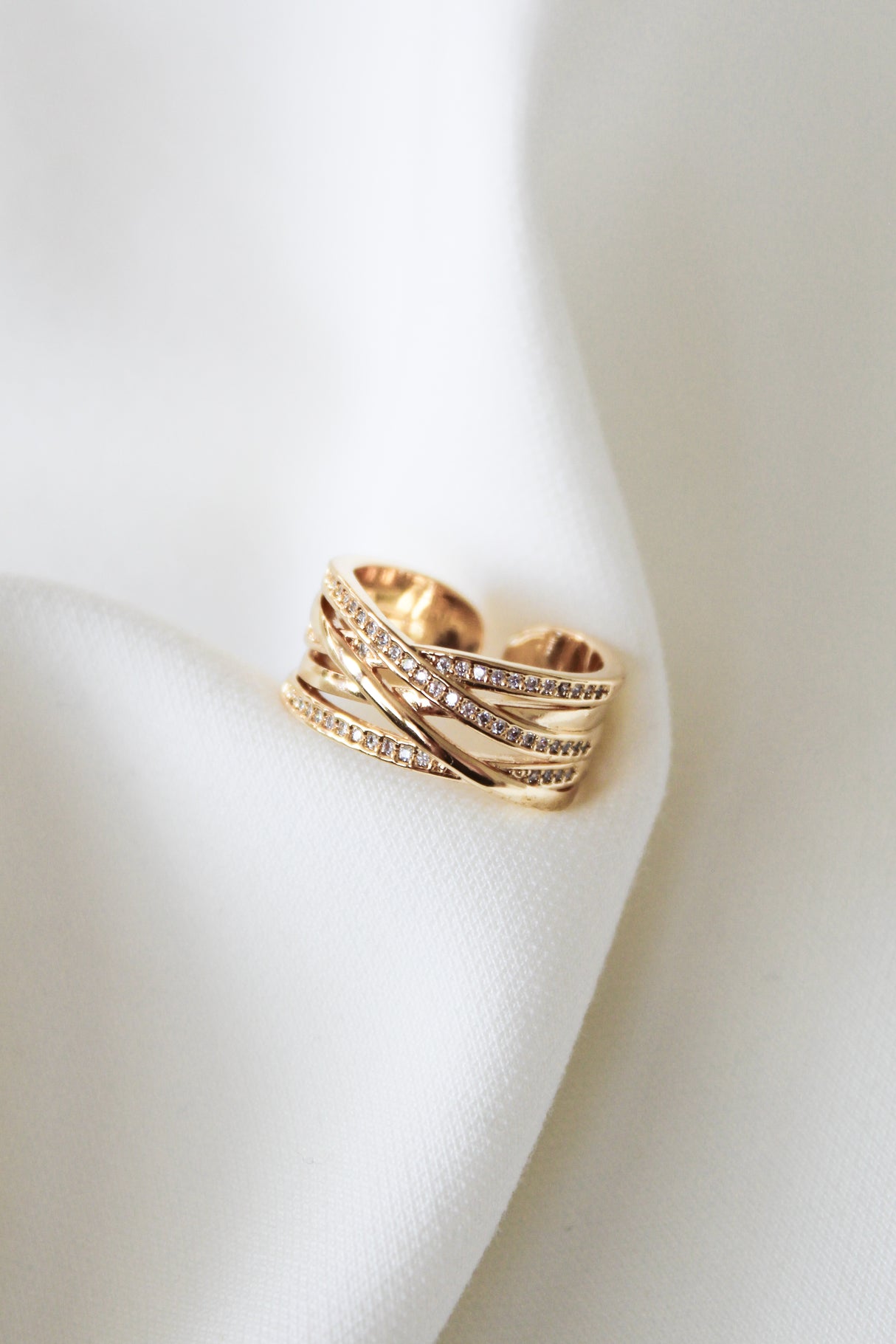 The Cris Ring by Kinsey Designs features multiple gold bands in a criss-cross design with small diamonds, making it a perfect anniversary gift or stacking ring, shown on white fabric.