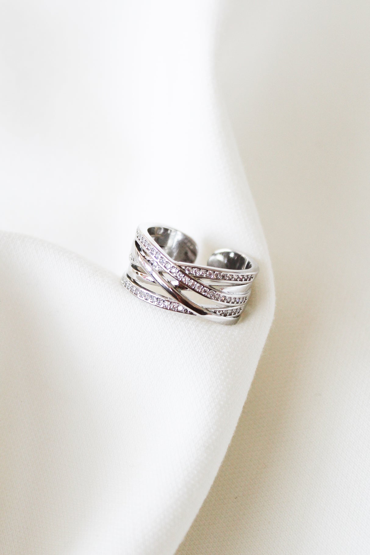 The Cris Ring by Kinsey Designs features stacked silver bands with small diamonds, displayed on white fabric—an elegant choice for an anniversary gift.