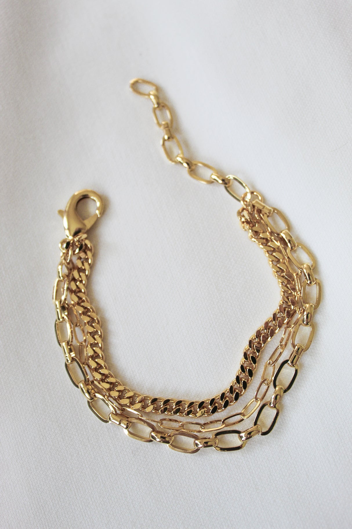 The Declan Bracelet from Kinsey Designs features three unique gold chains in 6" layers, shown on a white fabric background.