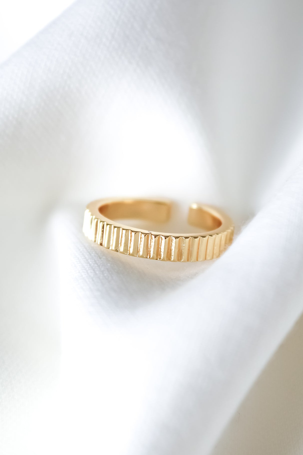 The Dillin Ring by Kinsey Designs—a gold filled, textured, adjustable piece—rests on soft white fabric with gentle folds and bright lighting. Discover it at our sample sale!.