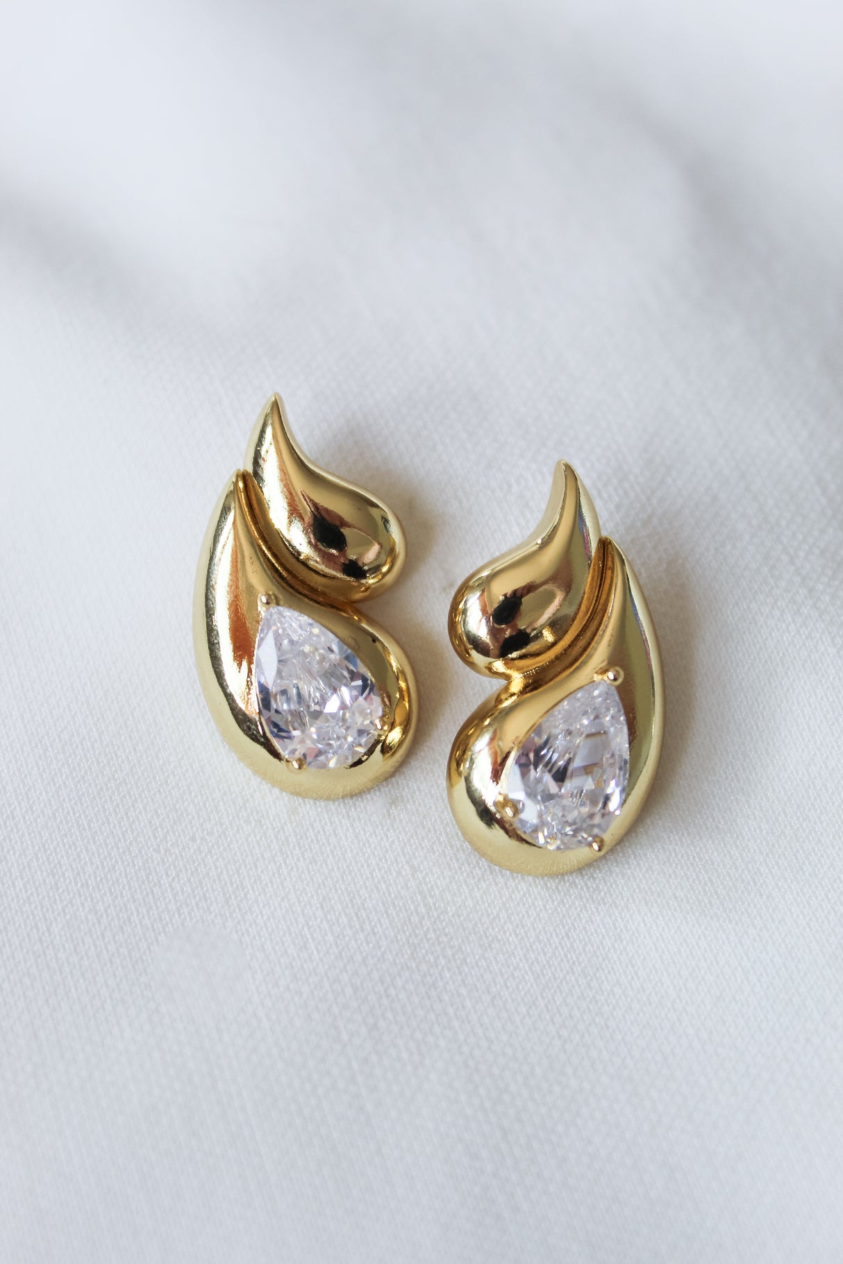 The Double Drop Stud by Kinsey Designs Archives features gold-filled teardrop shapes with clear gemstones, displayed on a white fabric background—an elegant addition to any jewelry collection.