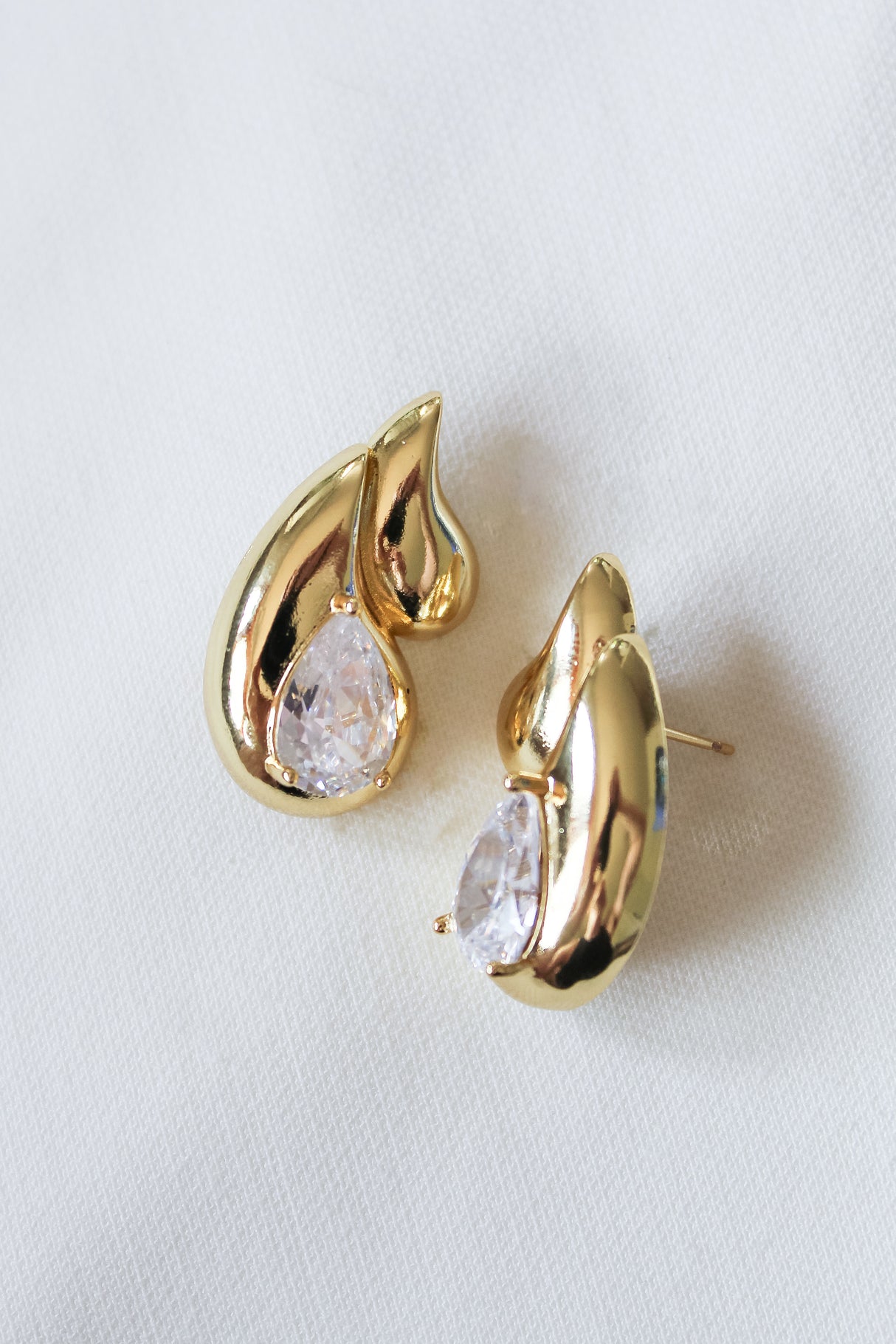 The Double Drop Stud by Kinsey Designs Archives features gold-filled teardrop earrings with clear gemstones, showcased on a white fabric background—ideal for elevating your jewelry collection or discovering a special piece at a sample sale.