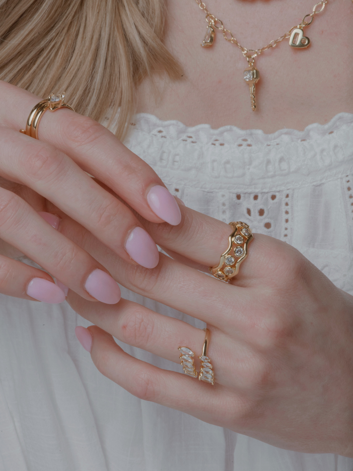 A woman in a white blouse wears the Kinsey Designs Dove Stacking Ring Set and a necklace, showing off her light pink manicured nails.