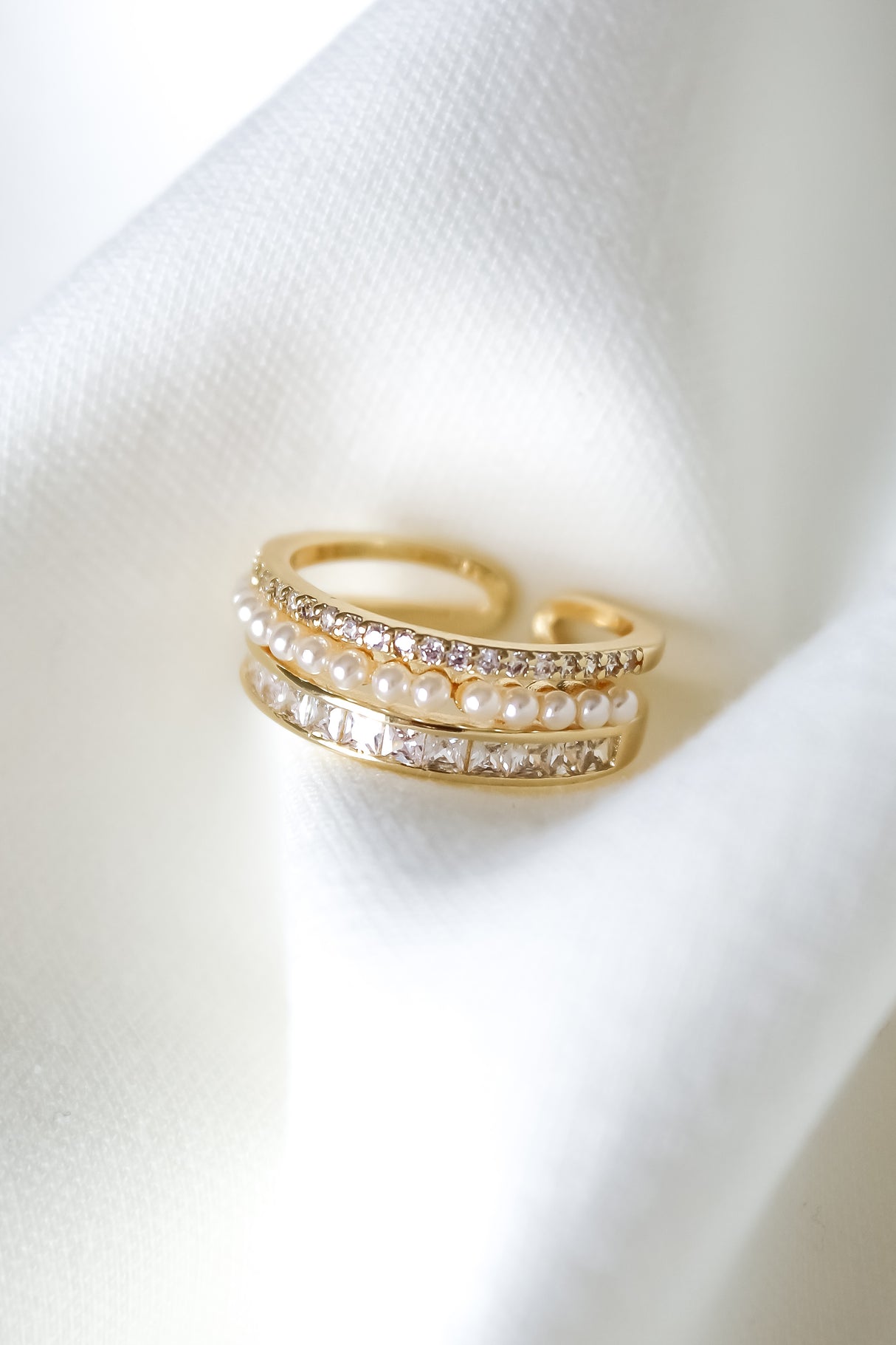 The Ellana Pearl Ring by Kinsey Designs features gleaming rows of pearls and diamonds on a crystal pavé band, showcased on soft white fabric.