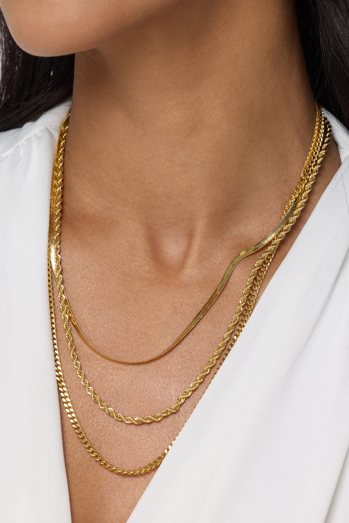 A woman wears a white top and the Emile Layer Necklace by Kinsey Designs Archives, a stunning multi-chain necklace that draws elegant focus to her neck and chest.
