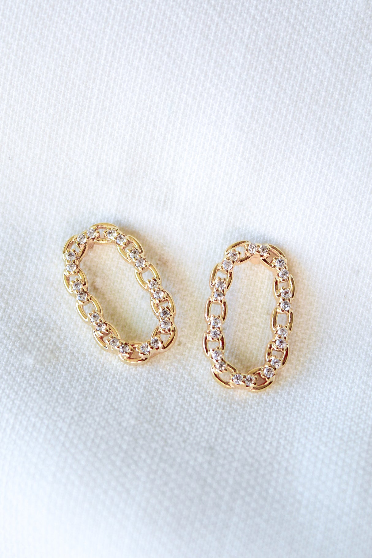 The Everly Post earrings by Kinsey Designs feature gold filled oval chain links and small diamonds, beautifully displayed on white textured fabric. Ideal for anyone seeking elegance at a sample sale price.