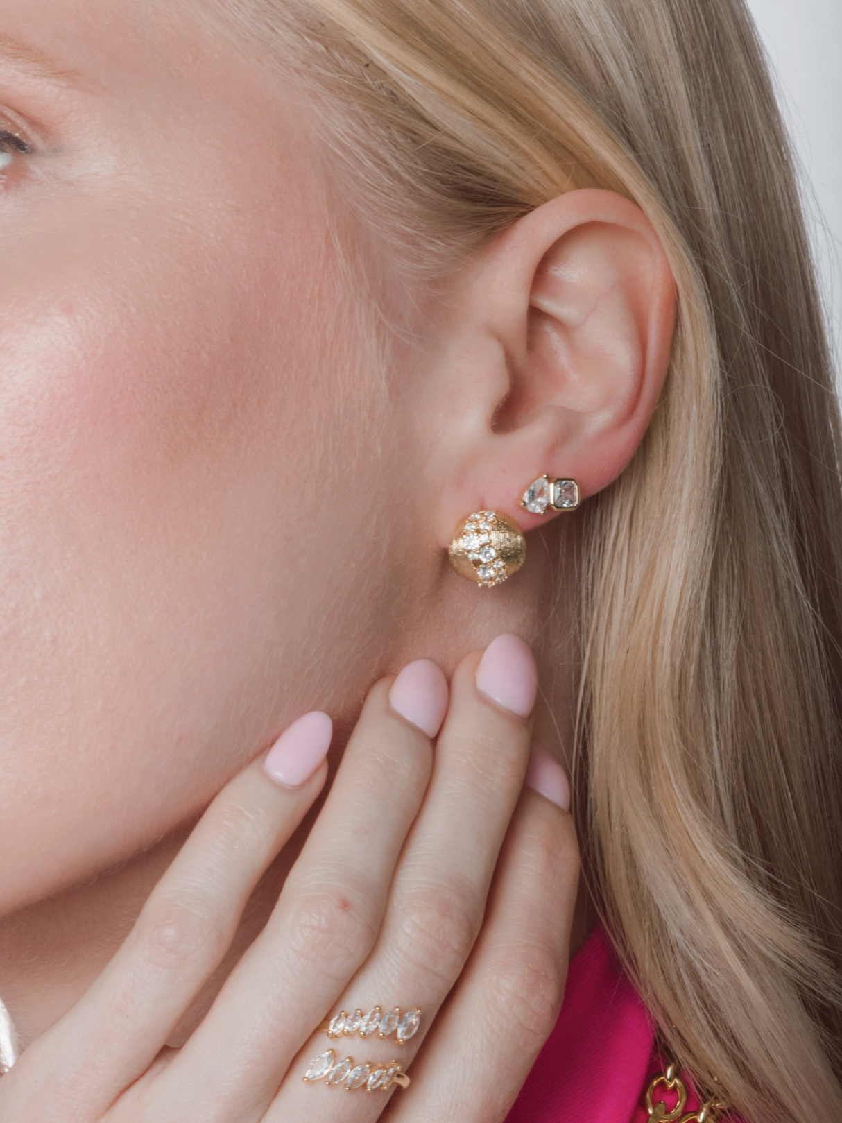 Close-up of a woman's ear wearing Kinsey Designs' Finn Post Earring, a gold round post with CZ, and her hand with pink nails featuring a diamond ring.