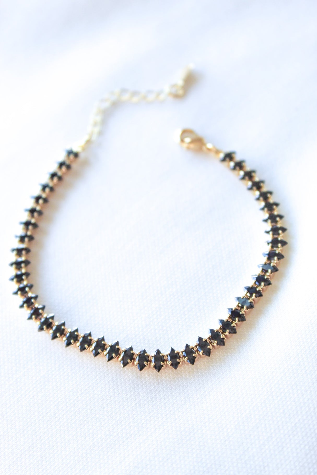 The Gator Mini Bracelet-Charcoal by Kinsey Designs Archives features gold plating and charcoal stones in a row, shown on white fabric. This item is part of our final sale.
