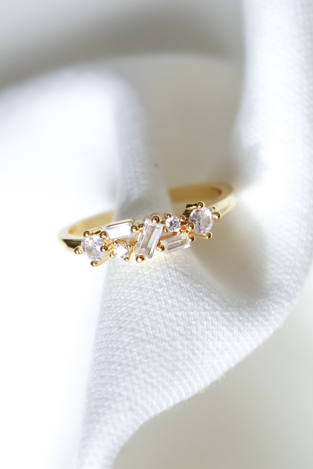 The Gavey Ring by Kinsey Designs Archives features small clear gemstones and is shown on a white textured fabric. Adjustable and perfect for stacking, this exclusive piece is available in our sample sale.
