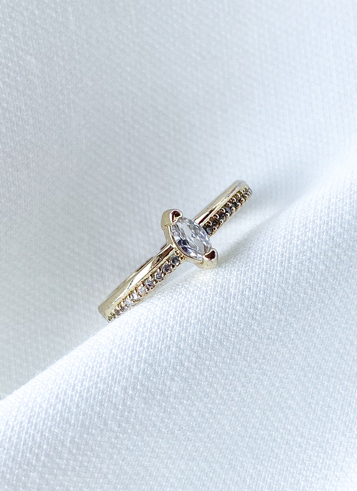 The Gideon Ring by Kinsey Designs features a gold-filled band with a marquise-cut diamond and small accent stones, elegantly displayed on white fabric.