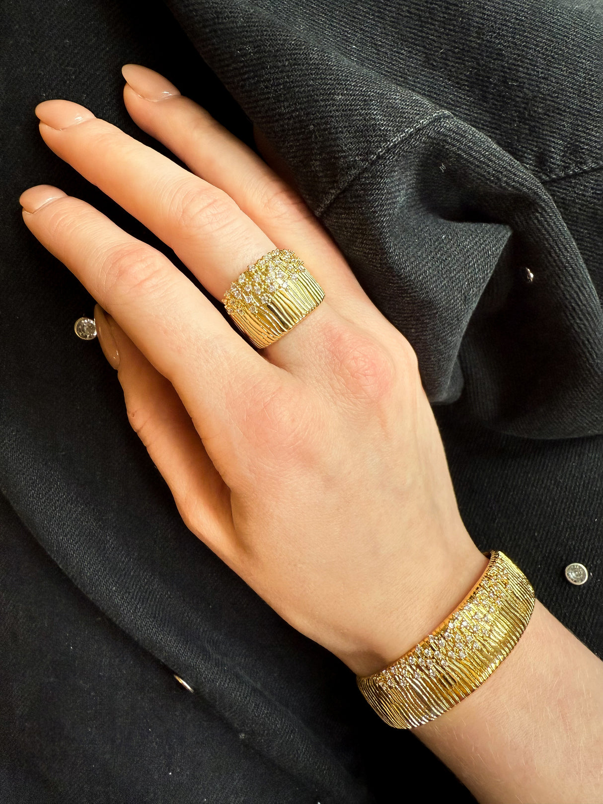 A hand wearing a gold ring and the Kinsey Designs Glinda Stardust Cuff Bracelet, featuring textured, sparkling designs with CZ accents, on dark fabric.