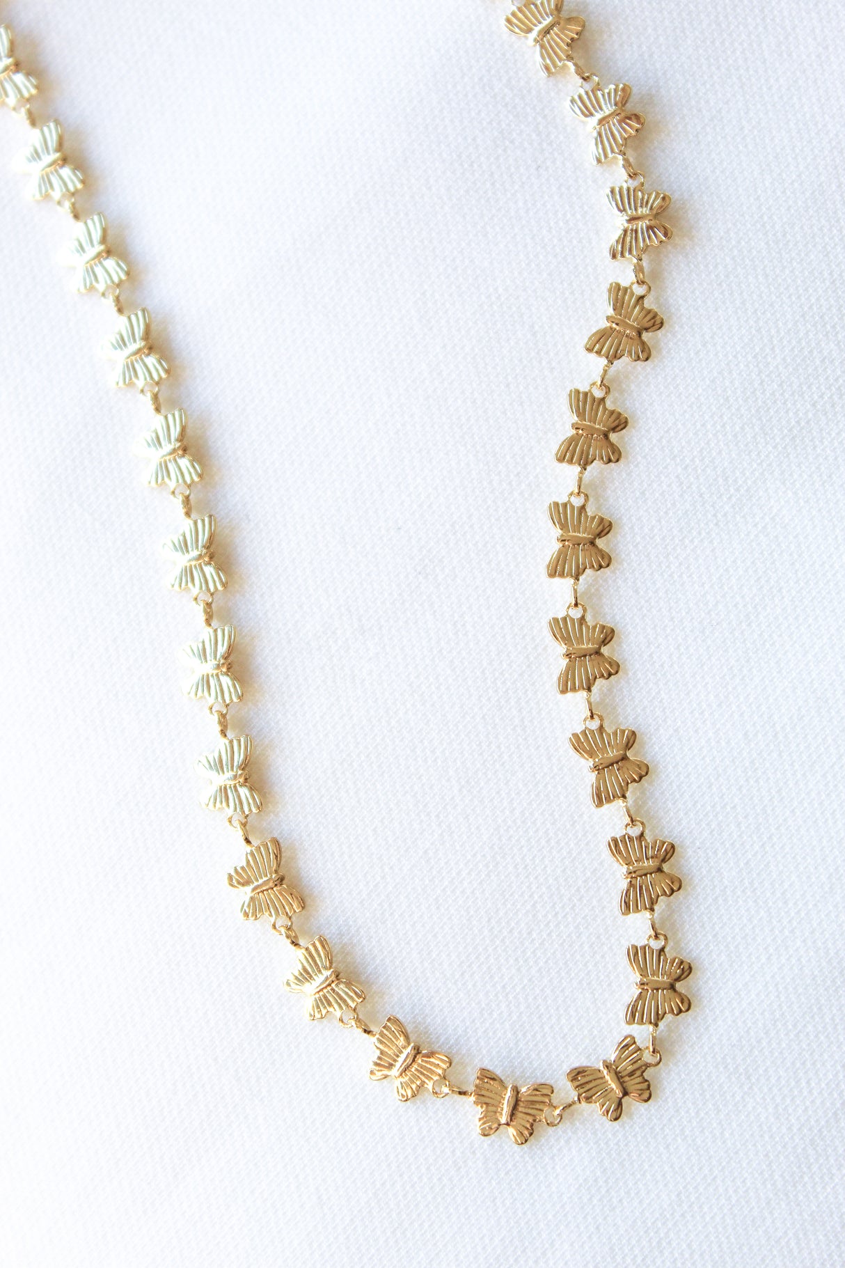 The Harper Necklace by Kinsey Designs Archives, a gold-filled butterfly-shaped piece, is displayed on a white textured fabric background.