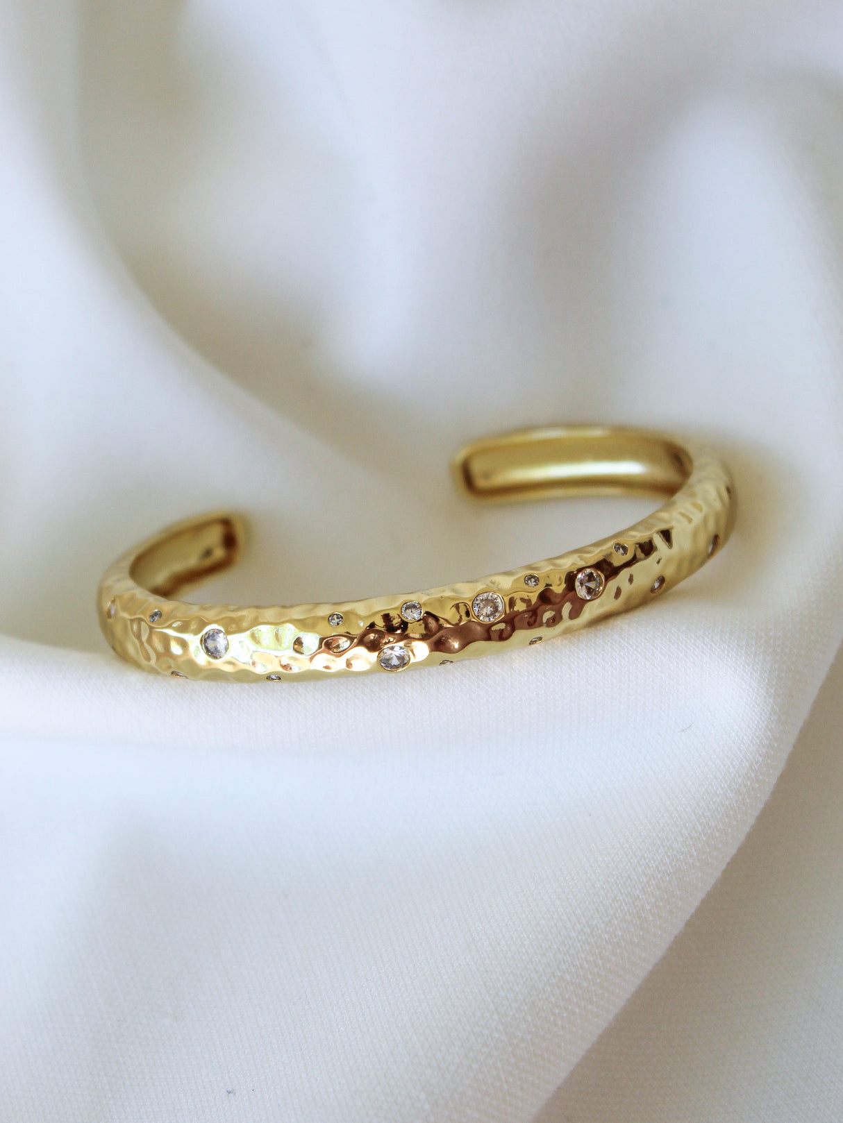 The Hartwell Cuff Bracelet by Kinsey Designs Archives features a hammered gold-filled finish with small gemstones, shown on white fabric. Elevate your style—shop this elegant piece at our sample sale!.