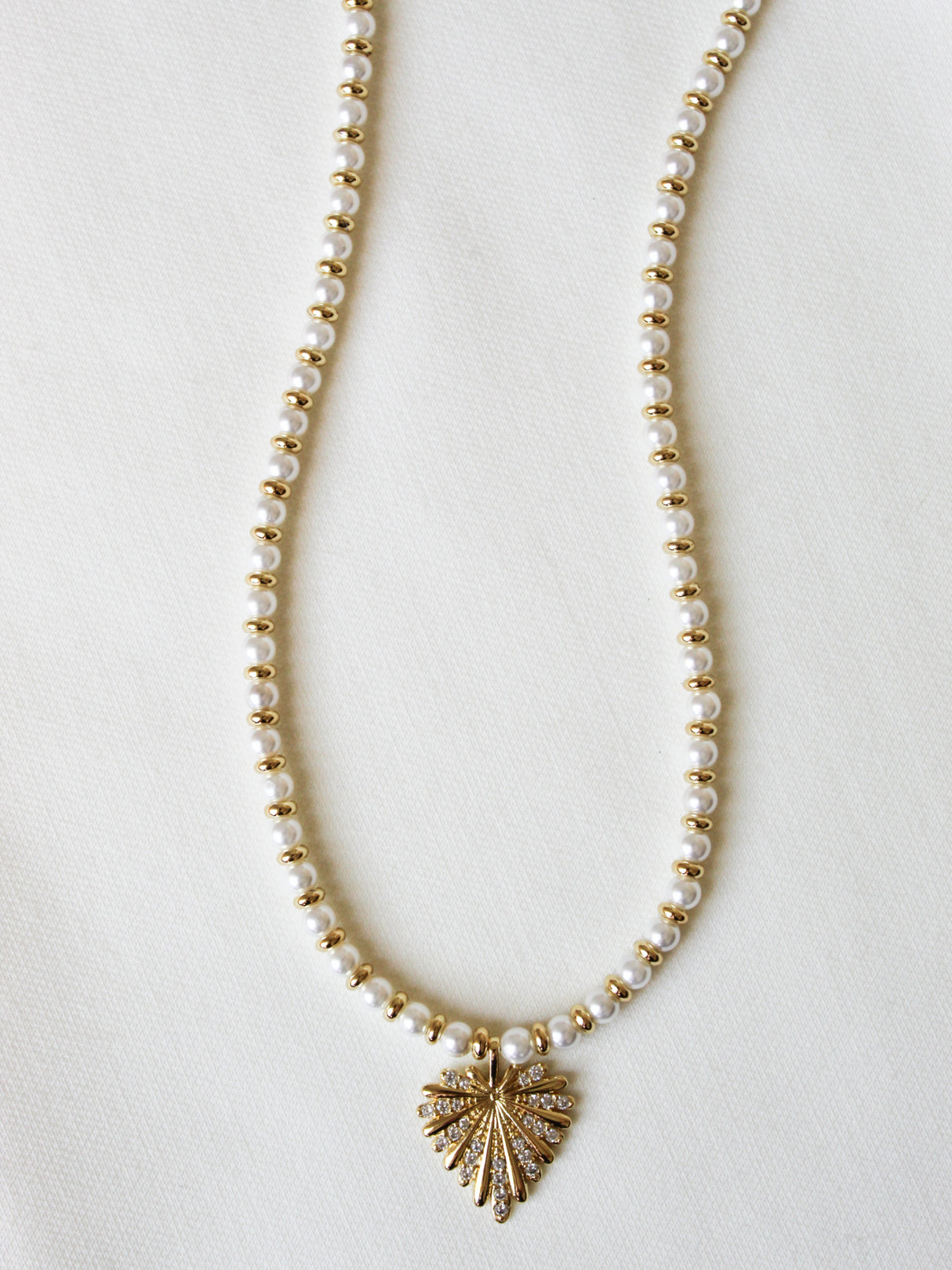 The Haven Necklace by Kinsey Designs is a gold-filled piece with pearl beads and a delicate gold leaf pendant, elegantly shown on a white fabric background.