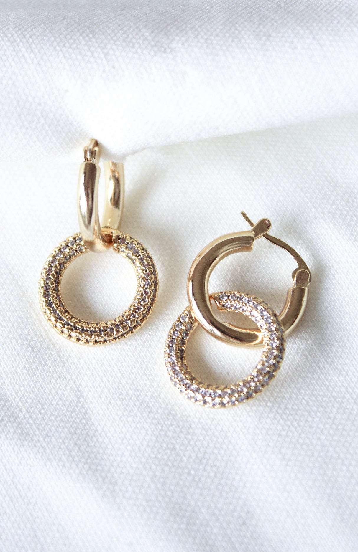 The Holland Hoop by Kinsey Designs features sparkling gold hoops, beautifully displayed on a soft white fabric background.