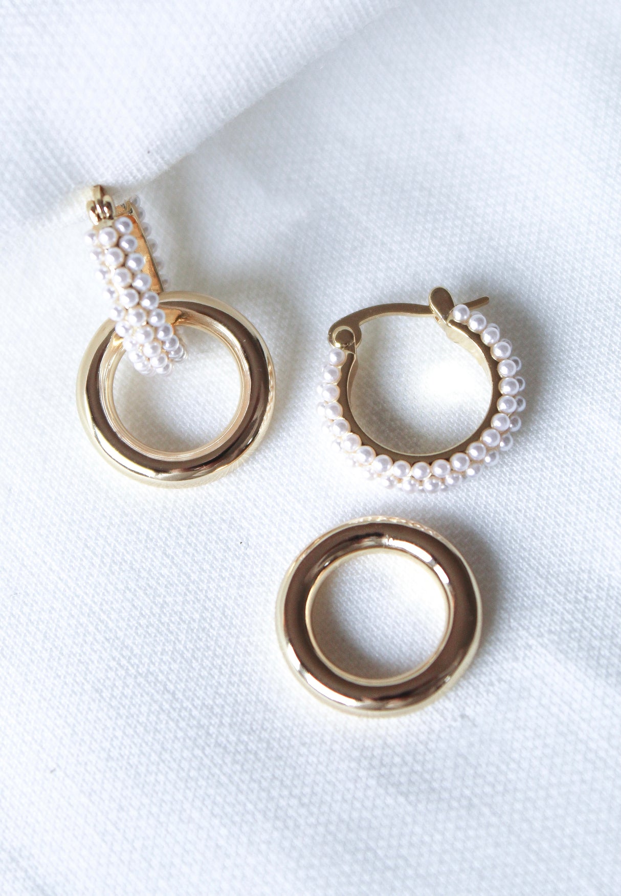 The Holland Pearl Hoops by Kinsey Designs feature gold filled hoops with small white pearls, elegantly displayed on a white textured fabric background.
