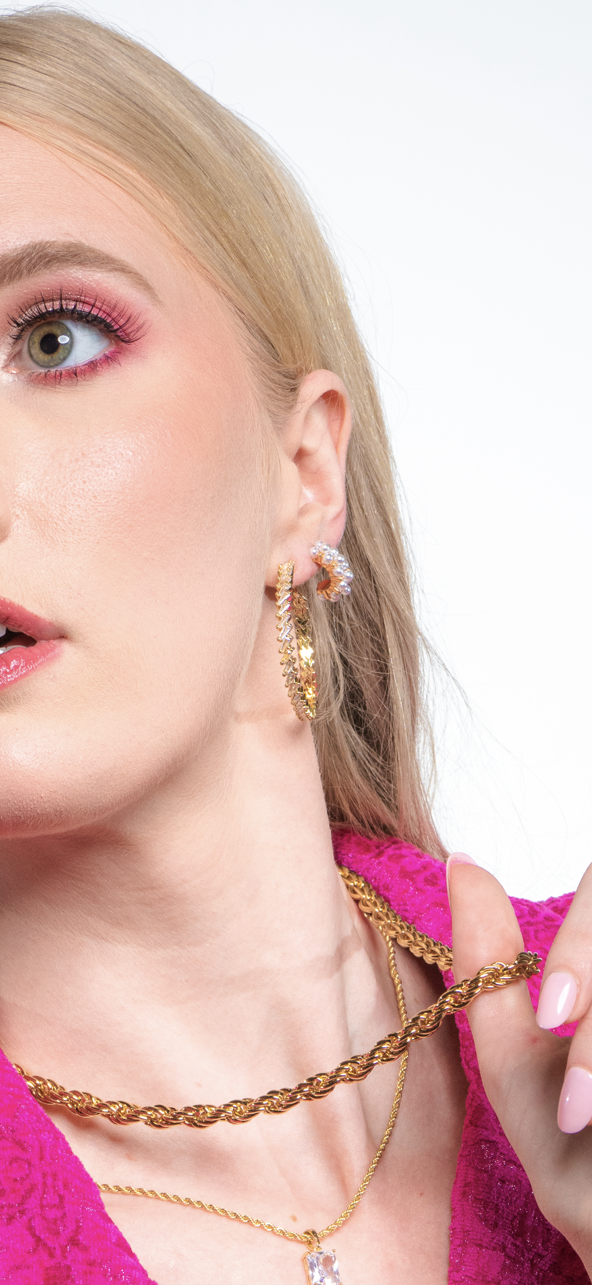 Close-up of a woman in a pink outfit and gold jewelry, wearing Kinsey Designs' Aeroine Pearl Hoops with blonde hair and pink eyeshadow, set against a white background.