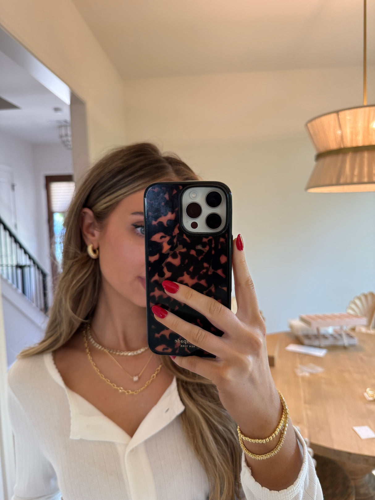 A woman takes a mirror selfie in a white top, wearing the Kinsey Designs Blaire Square Tennis Necklace and gold jewelry, her face hidden by her phone.